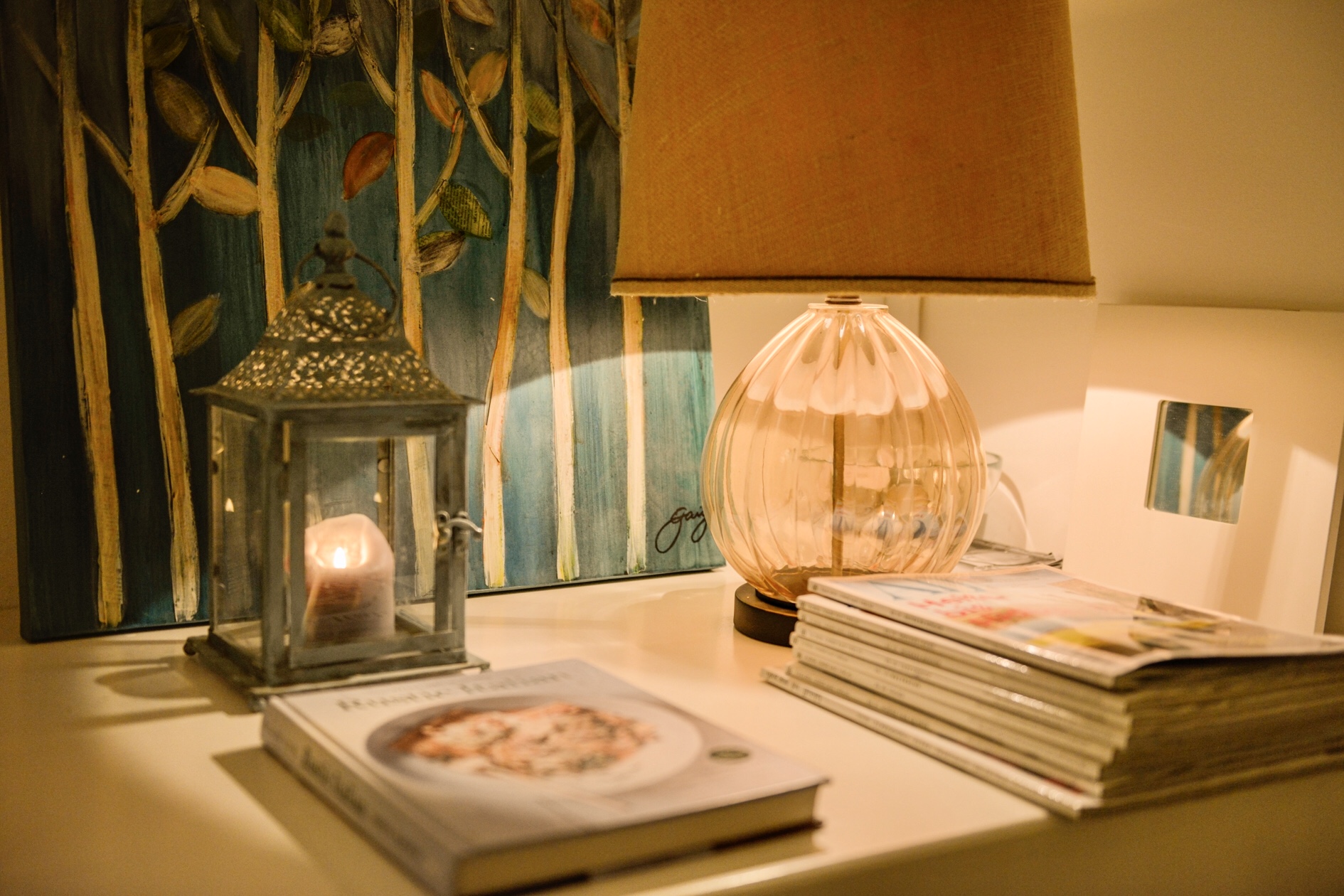 Lampada in vetro ambrato, lanterna e libri su un mobile della casa