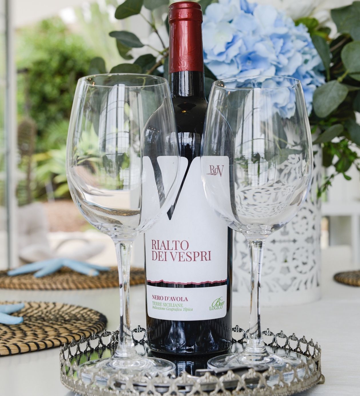 Bottiglia di Nero d'Avola e due calici su un vassoio in veranda