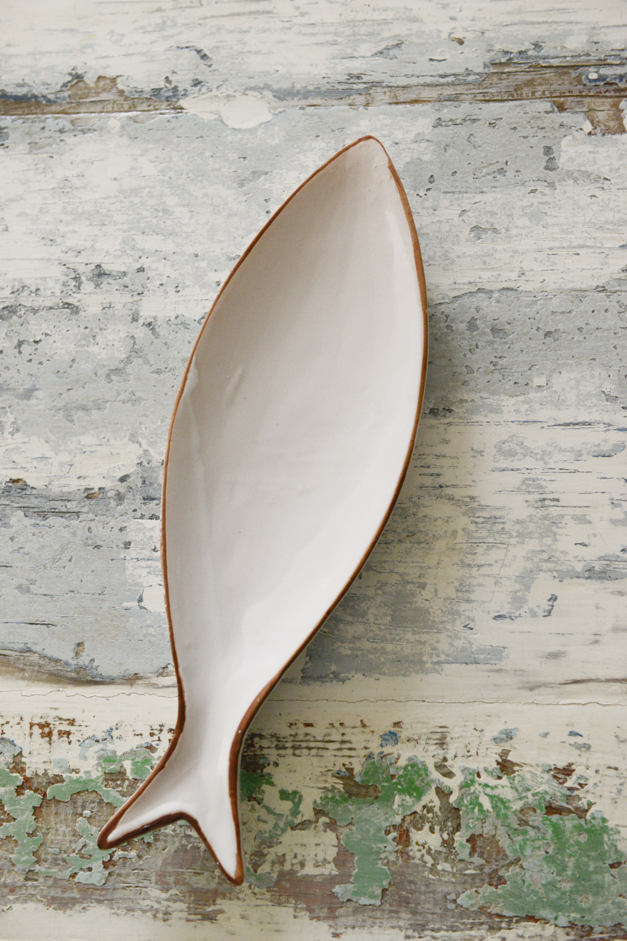 Piatto a forma di pesce in ceramica bianca su legno decapato