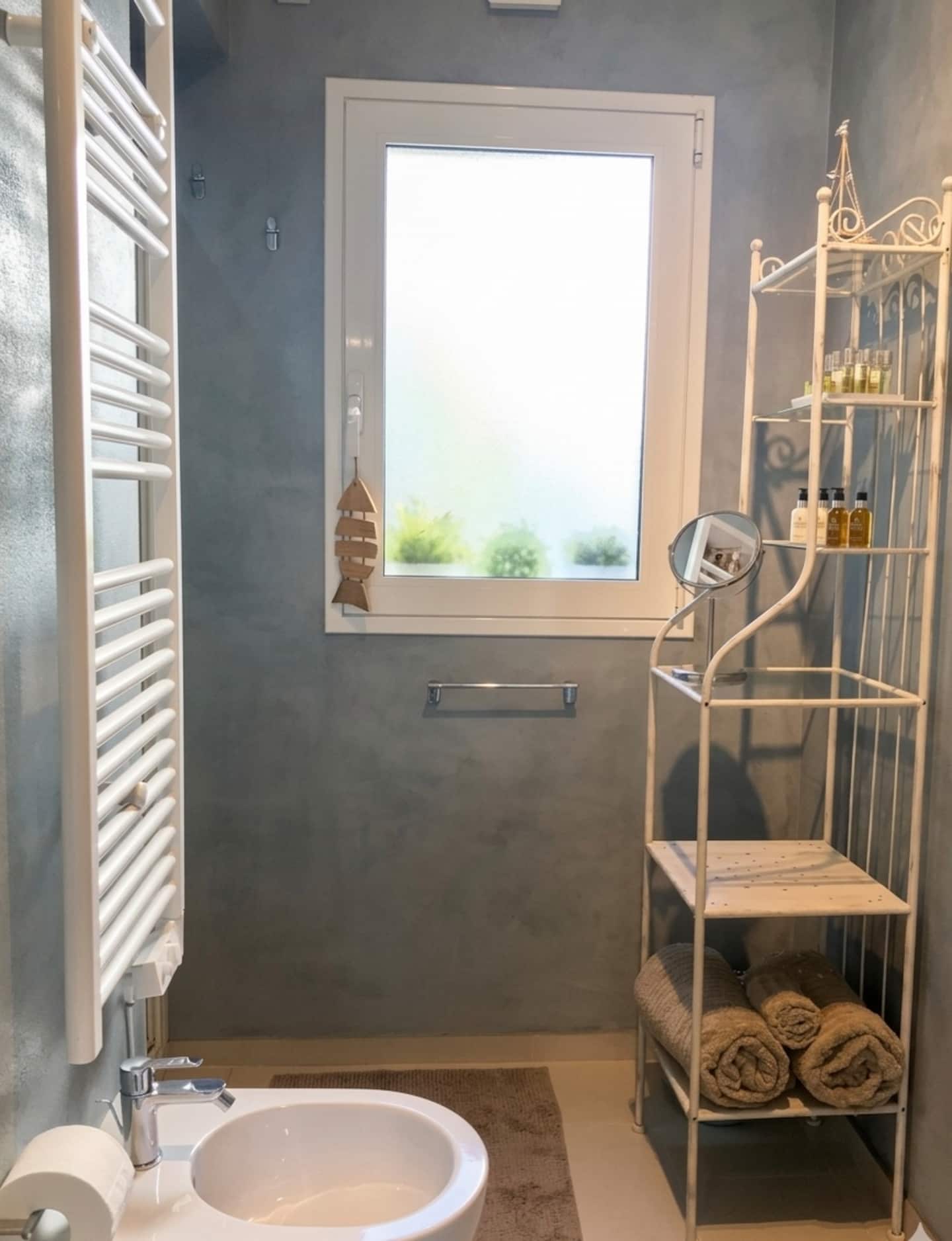 Bagno principale in cemento spatolato con finestra sul giardino